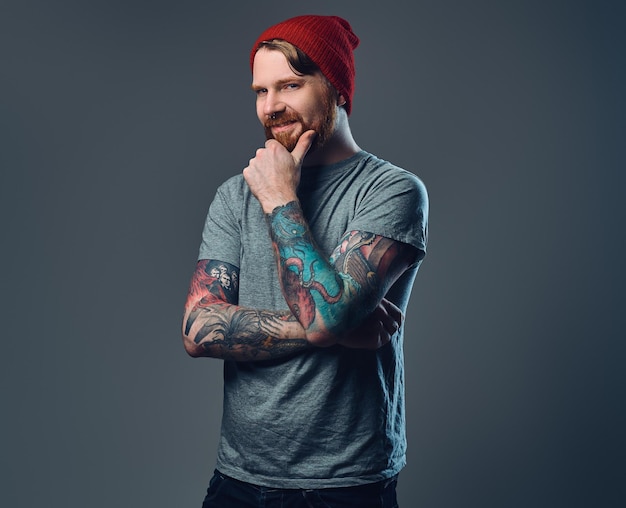 Free photo redhead bearded male with tattoos on his arms posing over grey background.