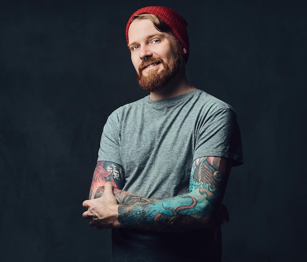 Бесплатное фото Рыжий бородатый мужчина с татуировками на руках позирует на сером фоне.