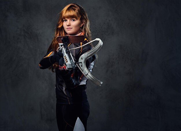 Redhead female Biathlon champion aiming with a competitive gun in a studio over grey background.Redhead female Biathlon champion aiming with a competitive gun in a studio over grey background.