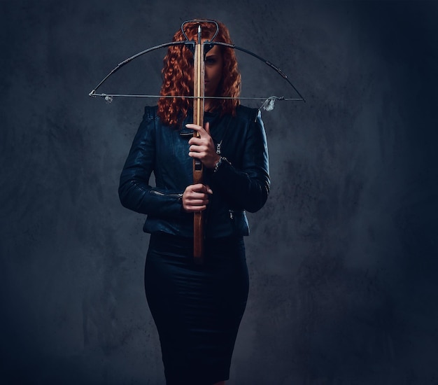 Free photo redhead female dressed in an elegant suit holds crossbow.