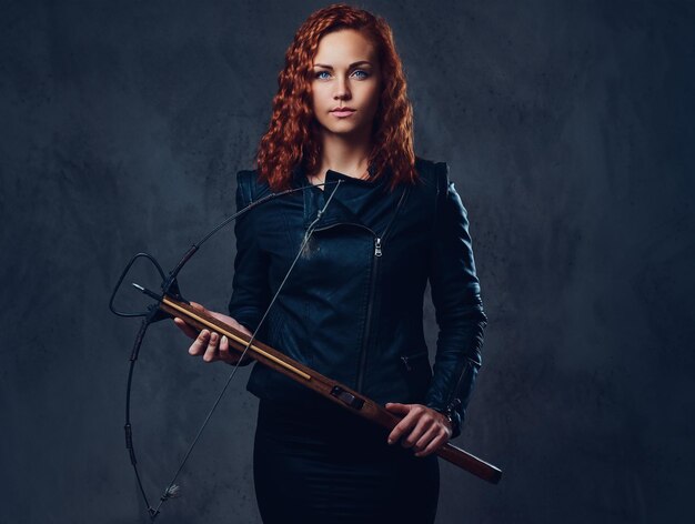 Redhead female dressed in an elegant suit holds crossbow.