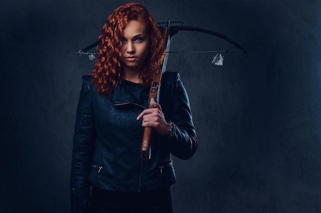 Free photo redhead female dressed in an elegant suit holds crossbow.