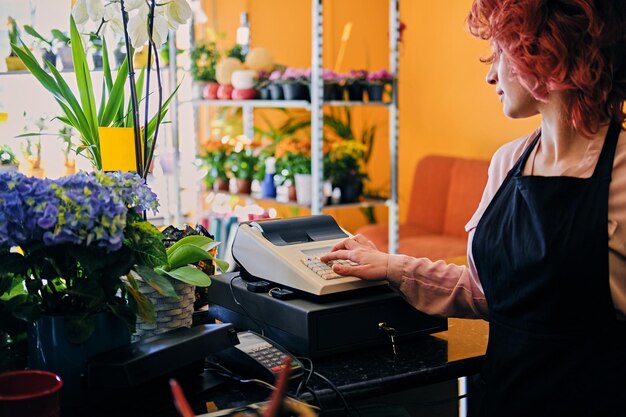 Redhead female flower seller using cash register in a market shop.