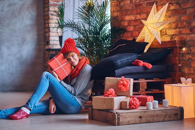 Redhead female holds a Christmas gift in a living room with loft interior.