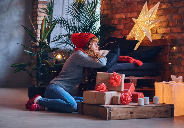 Redhead female holds a Christmas gift in a living room with loft interior.