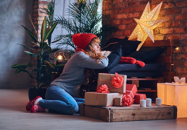 赤毛の女性は、ロフトのインテリアのリビングルームでクリスマスプレゼントを持っています。