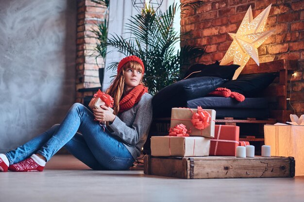 Redhead female holds a Christmas gift in a living room with loft interior.