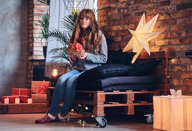 Redhead female holds a Christmas gift in a living room with loft interior.