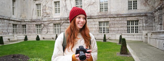 無料写真 赤毛の女の子の写真家が屋外でプロのカメラで写真を撮り、ストリート スタイルのショットをキャプチャします