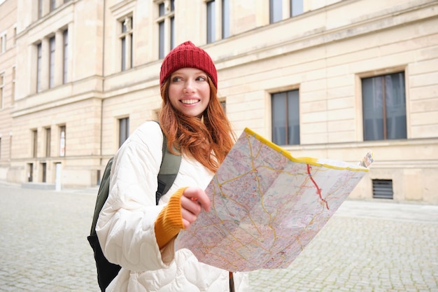 無料写真 赤毛の女の子の観光客が街を探索し、紙の地図を見て、歴史的建造物の女性の道を見つける