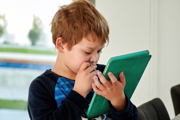 Redhead kid boy playing games on tablet