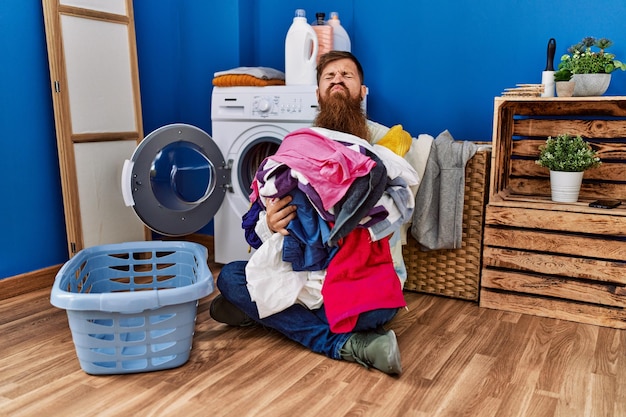 Redhead man with long beard putting dirty laundry into washing machine looking at the camera blowing a kiss being lovely and sexy love expression