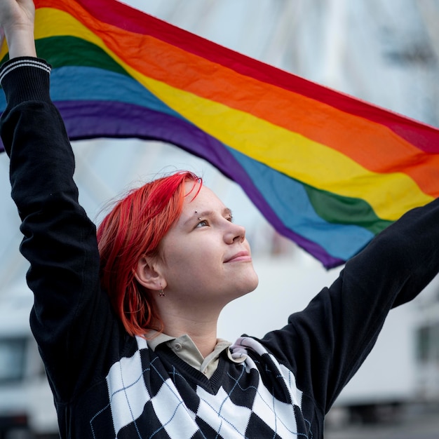 Redhead non binary person holding up a lgbt flag