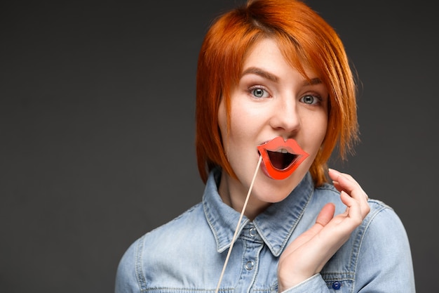 Redhead silly woman holding fake lips and smiling