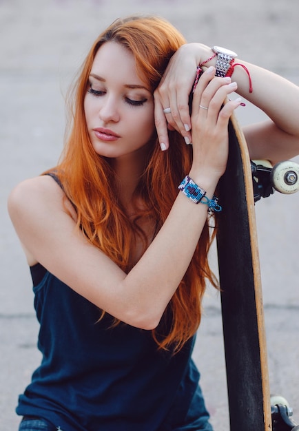 Redhead slim girl in jeans shorts and black t shirt posing with skateboard in urban sciene.