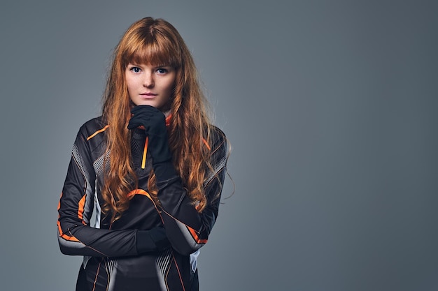 A redhead sporty female dressed in a winter sportswear isolated on grey background.