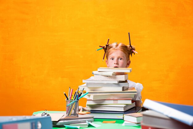 Foto gratuita la ragazza teenager rossa con molti libri a casa. colpo dello studio