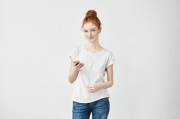 redhead woman in headphones smiling holding phone.