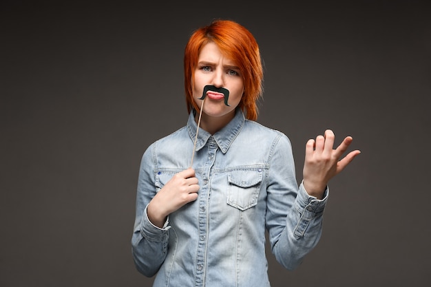 Free photo redhead woman holding fake moustache grimacing