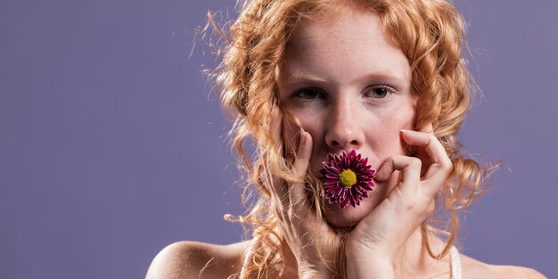 Redhead woman posing with a chrysanthemum on her mouth and copy space