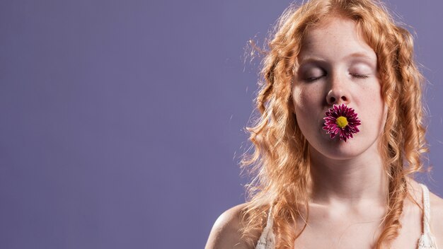赤毛の女性が彼女の口とコピースペースに花でポーズ