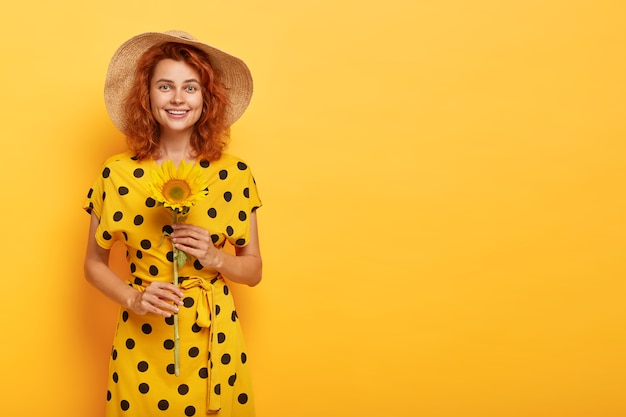 redhead woman posing in yellow polka dress and straw hat