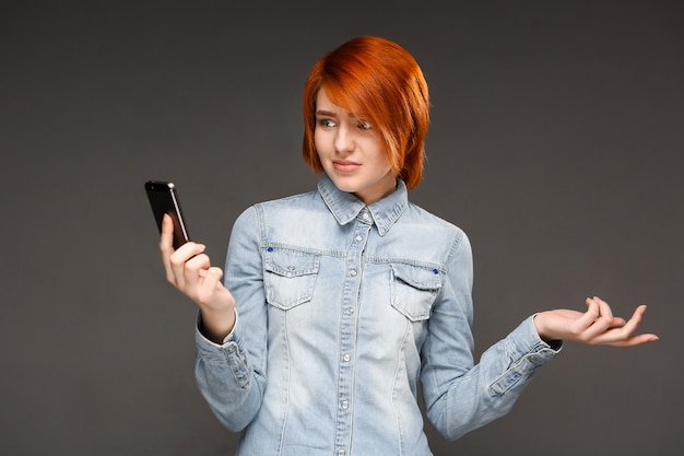 Foto gratuita fissare della donna della testarossa confuso sul telefono cellulare