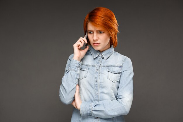 Redhead woman talking confused on mobile phone