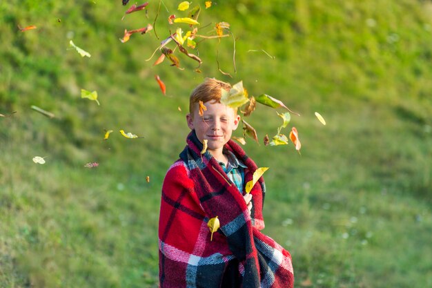 Рыжий мальчик играет с листьями