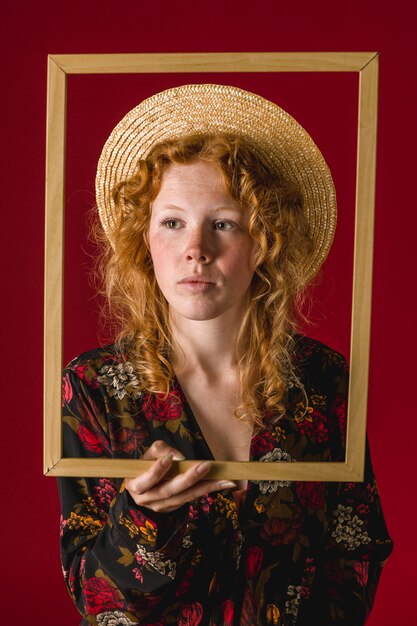 Redhead young female holding wooden frame