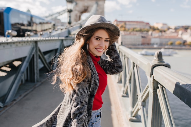 Утонченная девушка в элегантном твидовом пальто позирует с очаровательной улыбкой на городском фоне во время путешествия