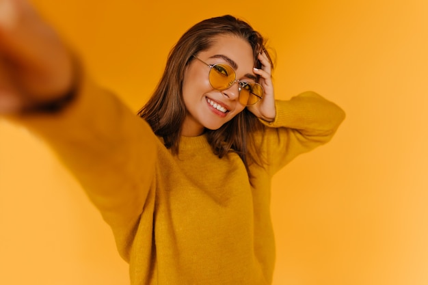 Free photo refined tanned woman with gorgeous smile making selfie. indoor shot of appealing brunette girl in autumn sweater.