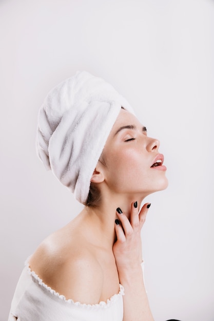 Refined woman enjoying herself during morning routine. Portrait of lady in towel on an isolated wall.