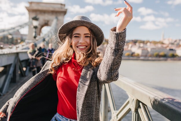 Refined woman in trendy gray coat having fun during photoshoot on bridge