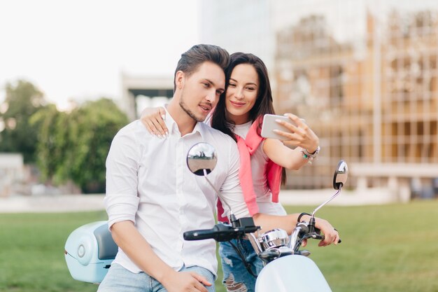 Refined woman with black hair and cute smile making selfie with boyfriend on date in summer weekend