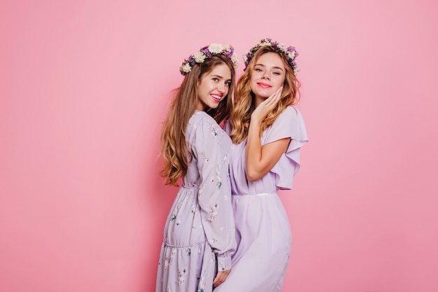 Refined woman with blonde wavy hair posing with sister on pink wall