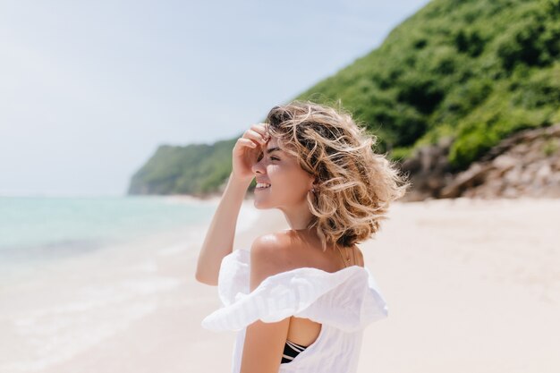 바다를보고 짧은 빛 머리를 가진 세련 된 젊은 여자. 해변 주위를 산책하는 사랑스러운 검게 여자의 야외 초상화.