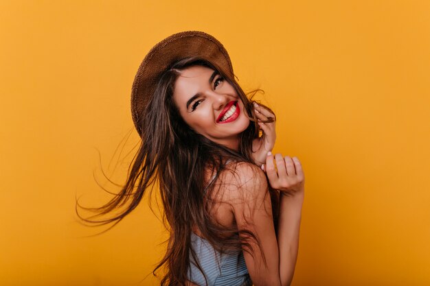 Refined young woman with tanned skin looking over shoulder with sincere laugh