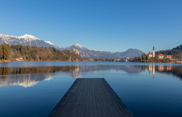 Reflection of the mountains and old buildings in the lake with a wooden pier in the foreground