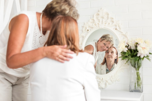 Free photo reflection of senior mother and mature daughter on mirror at home