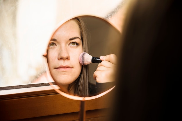 Reflection of a woman applying blusher on her face