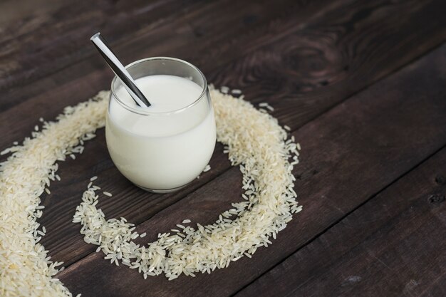 Refreshing rice milk in glass with straw placed in circular frame of raw rice over background