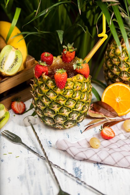 Освежающий летний алкогольный коктейль Маргарита с колотым льдом и цитрусовыми внутри ананаса с клубникой на кухонном столе