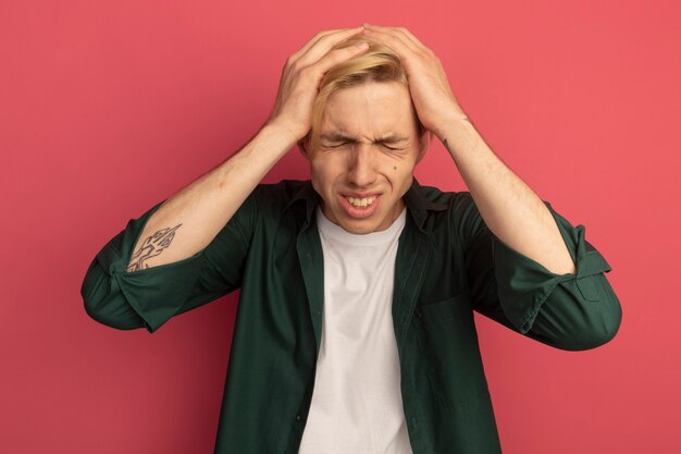 Regretted with closed eyes young blonde guy wearing green t-shirt grabbed head