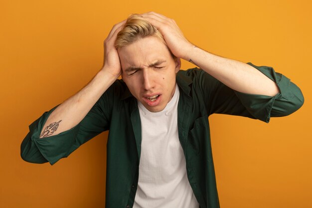 Free photo regretted with closed eyes young blonde guy wearing green t-shirt grabbed head