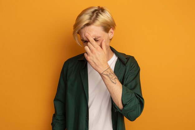 Regretted with closed eyes young blonde guy wearing green t-shirt putting hand on forehead