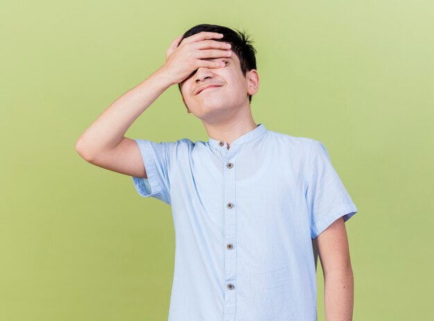 Regretting young caucasian boy keeping hand on forehead with closed eyes isolated on olive green background