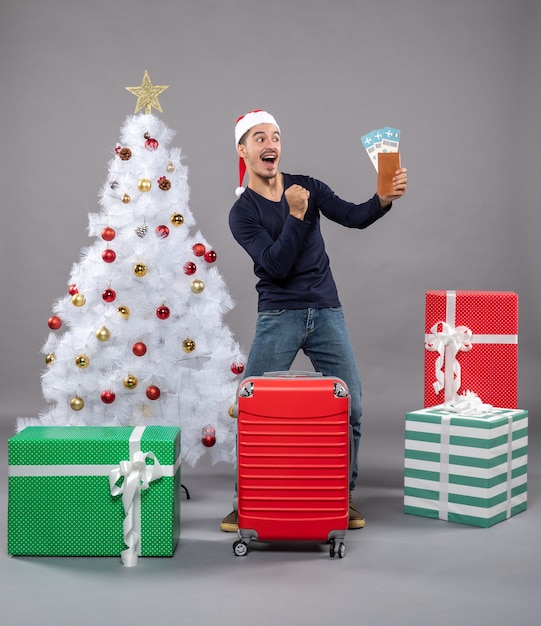 rejoiced man holding his travel tickets near xmas tree on grey