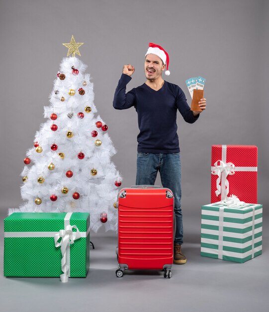 rejoiced man with suitcase holding his travel tickets on grey