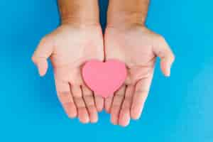 Free photo relationship concept on blue table flat lay. hands holding paper cut heart.